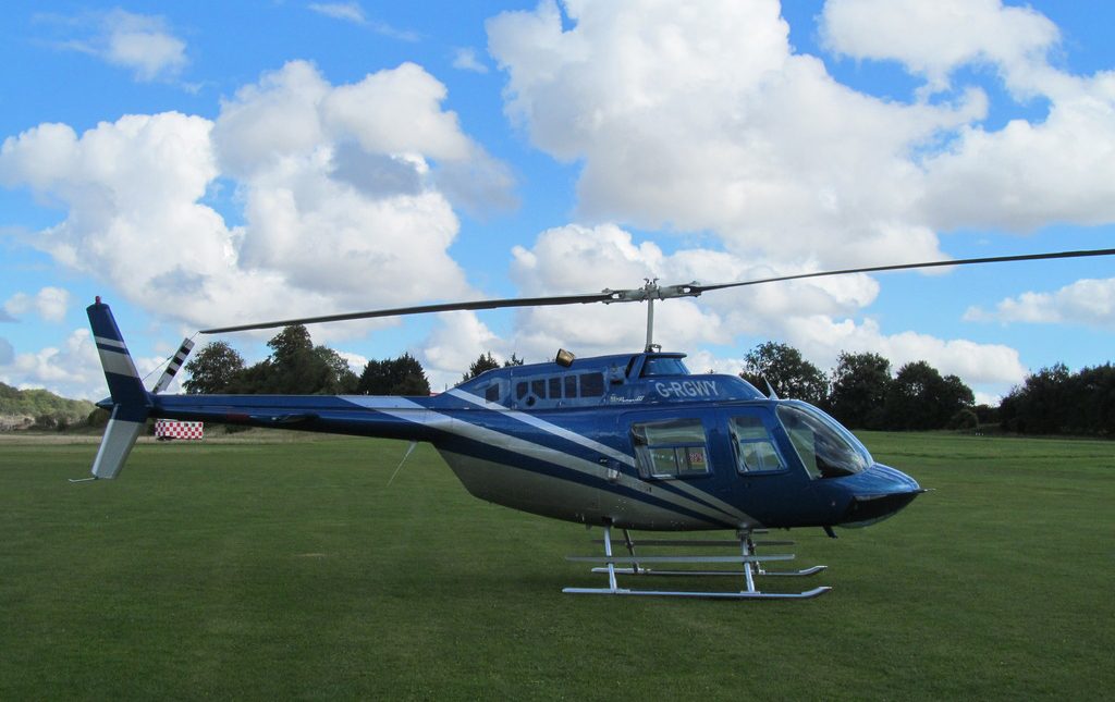 An image of a blue single-bladed helicopter landing on a green turf